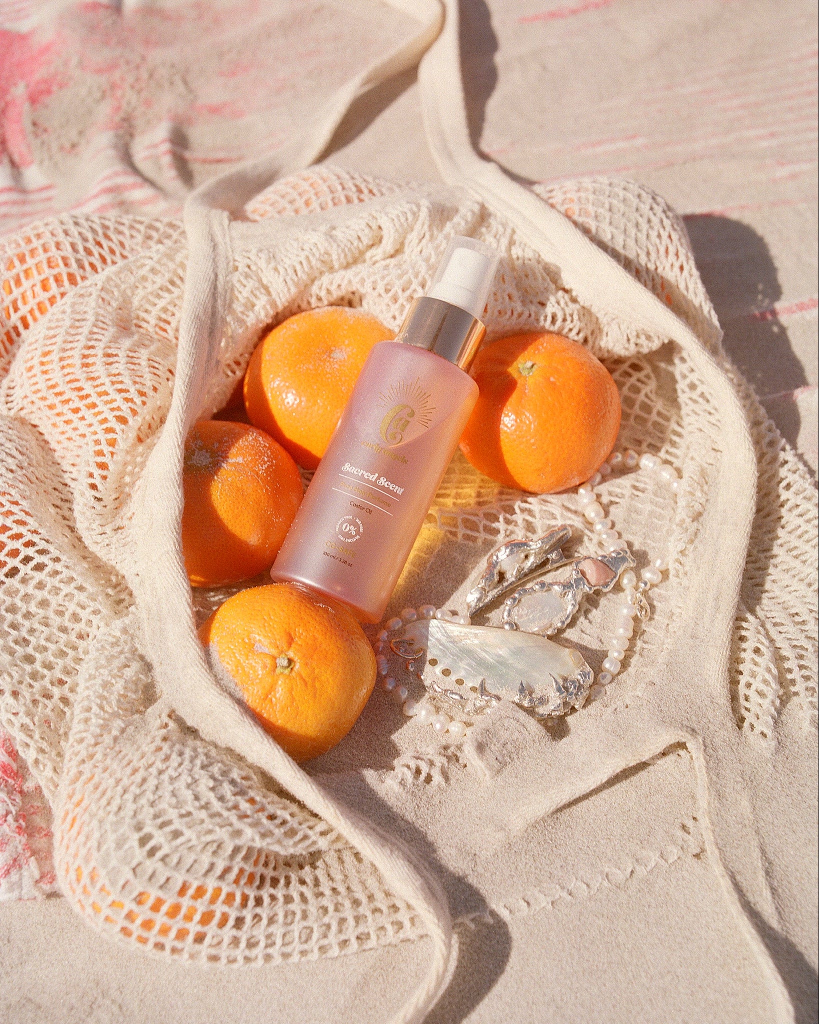 curly angels sacred scent hair mist resting agaainst a cotton bag of mandarins on a beach with scattered freshwater pearl jewellery - vegan - cruelty-free - curly girl method safe