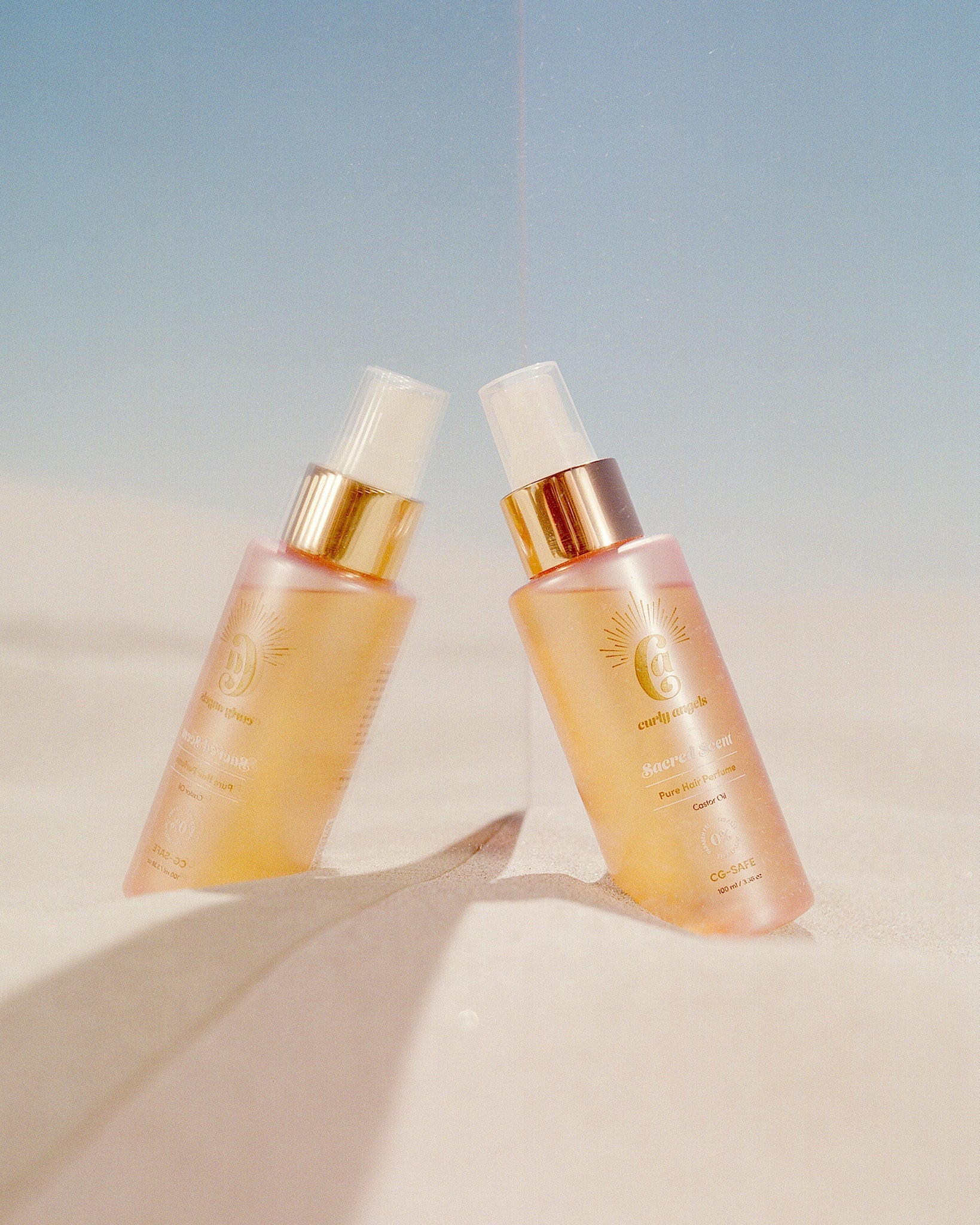 Curly Angels Sacred Scent Hair Mist on a mirror set in beach sand and clear blue sky - vegan - cruelty-free - Curly Girl Method Safe 
