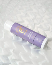 A bottle of Salvation Conditioner by Curly Angel resting on a bed of wavy shampoo designed to deeply nourish and hydrate