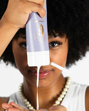A model with Afro squeezing a bottle of vegan Salvation Conditioner by Curly Angel designed deeply nourish and hydrate all curly hair types