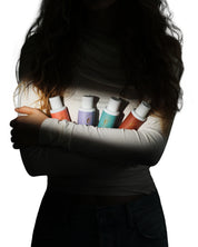 Model in Shadow Holding a set of Curly Angels to Goo Travel size haircare bottles
