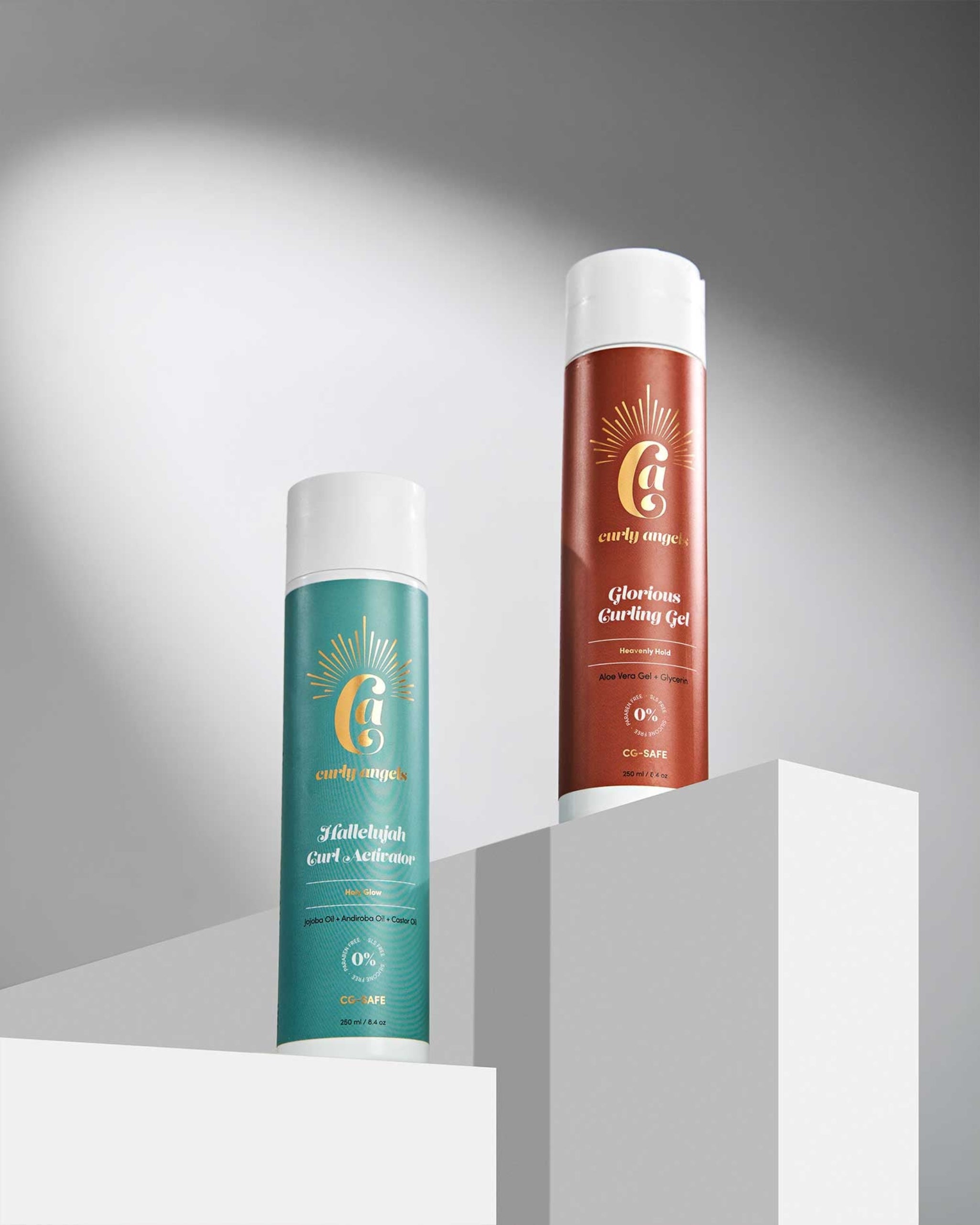 Two bottles of Curly Angels styling products, Hallelujah Curl Activator and Glorious Curling Gel on white plinths