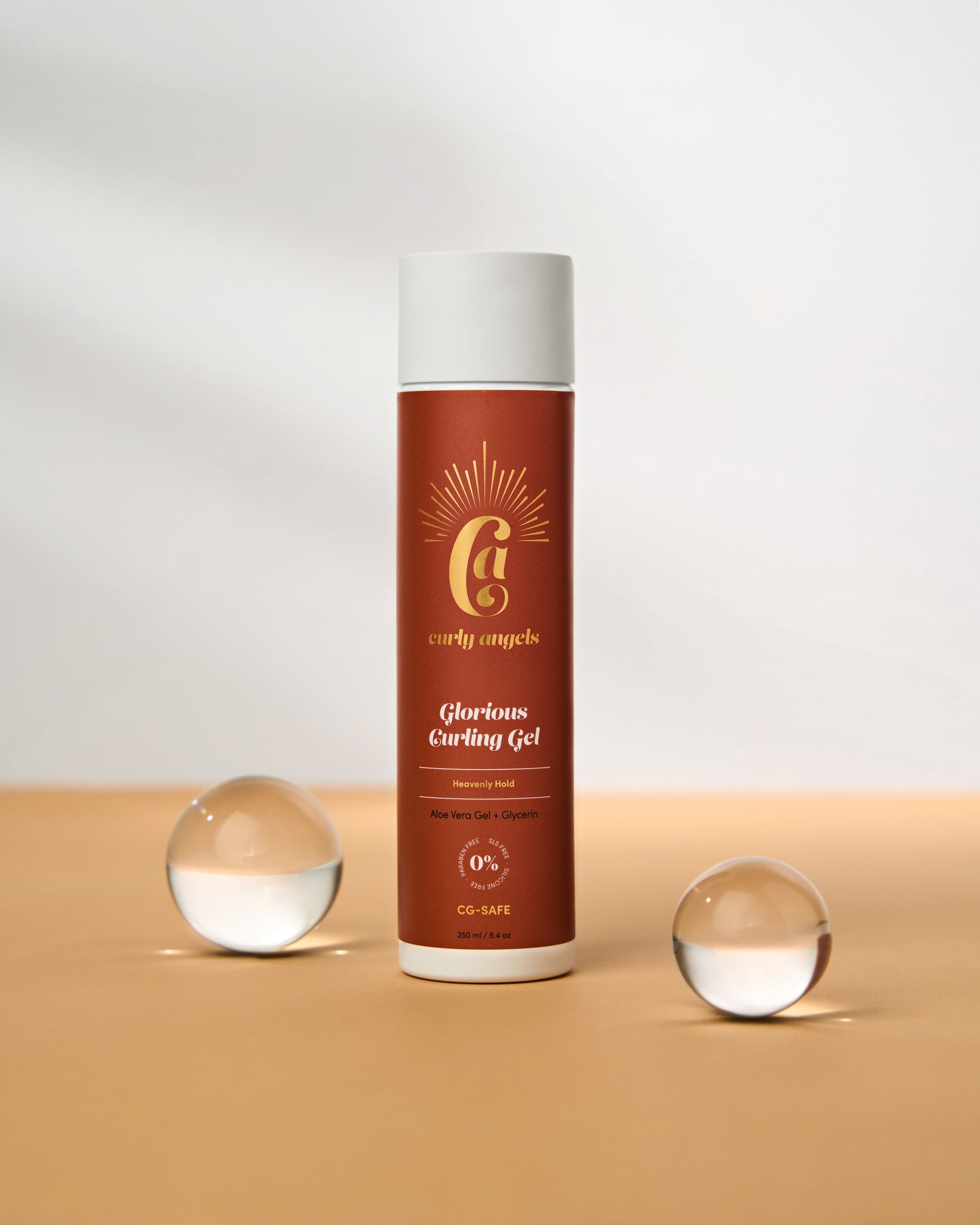 A bottle of Curly Angels Vegan Glorious Curling Gel with two decorative glass balls in front, set against a neutral background.