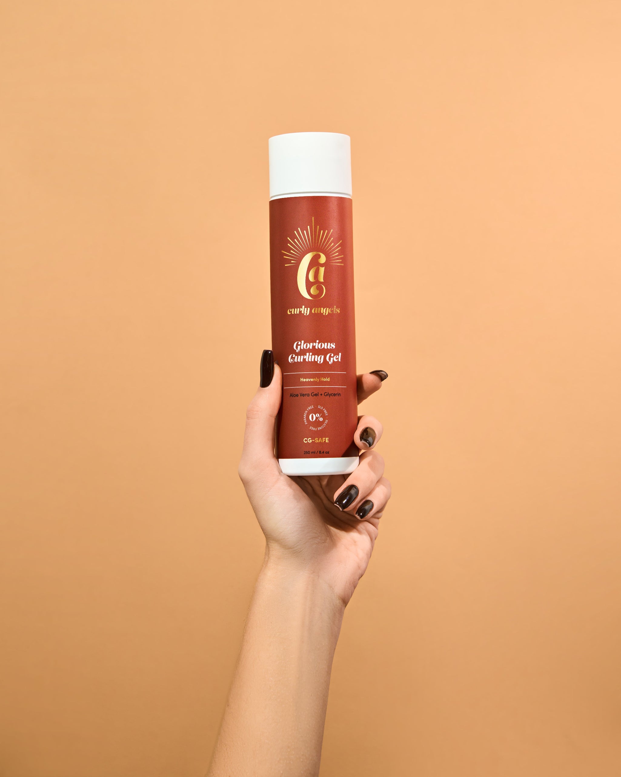 A hand holding a bottle of Curly Angels vegan Glorious Curling Gel against an orange background.