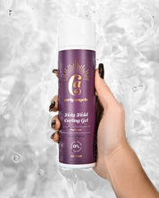 A hand holding a bottle of Curly Angel Holy Hold Curling Gel with strong hold, against a water droplets background.