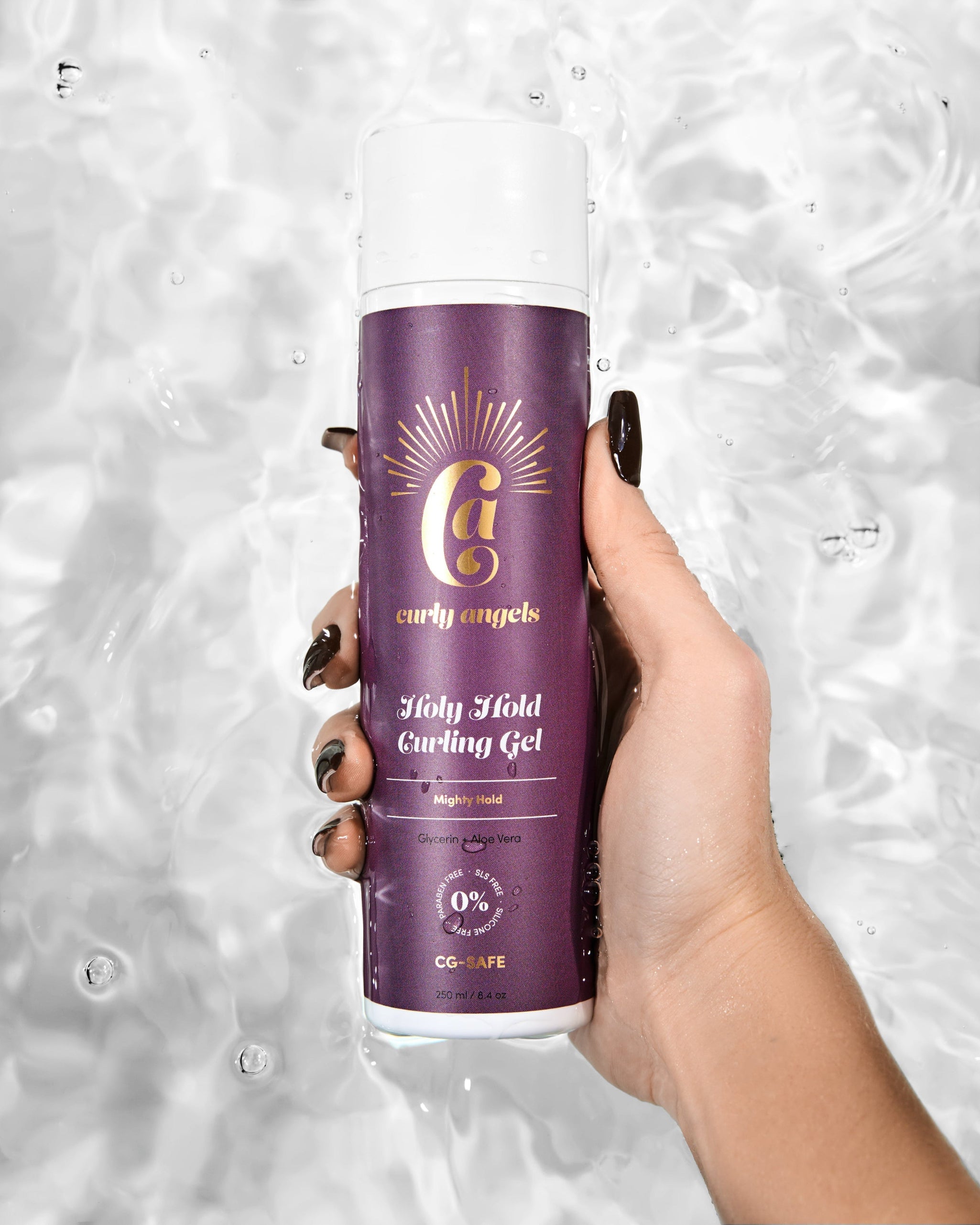 A hand holding a bottle of Curly Angel Holy Hold Curling Gel with strong hold, against a water droplets background.